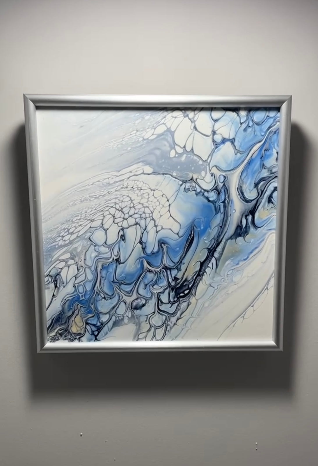 Framed abstract artwork with blue and white colors on a gray wall