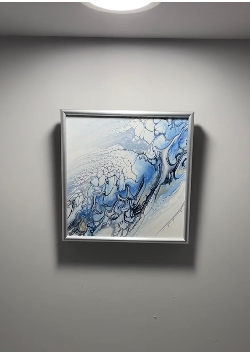 Framed abstract artwork with blue and white colors on a gray wall.